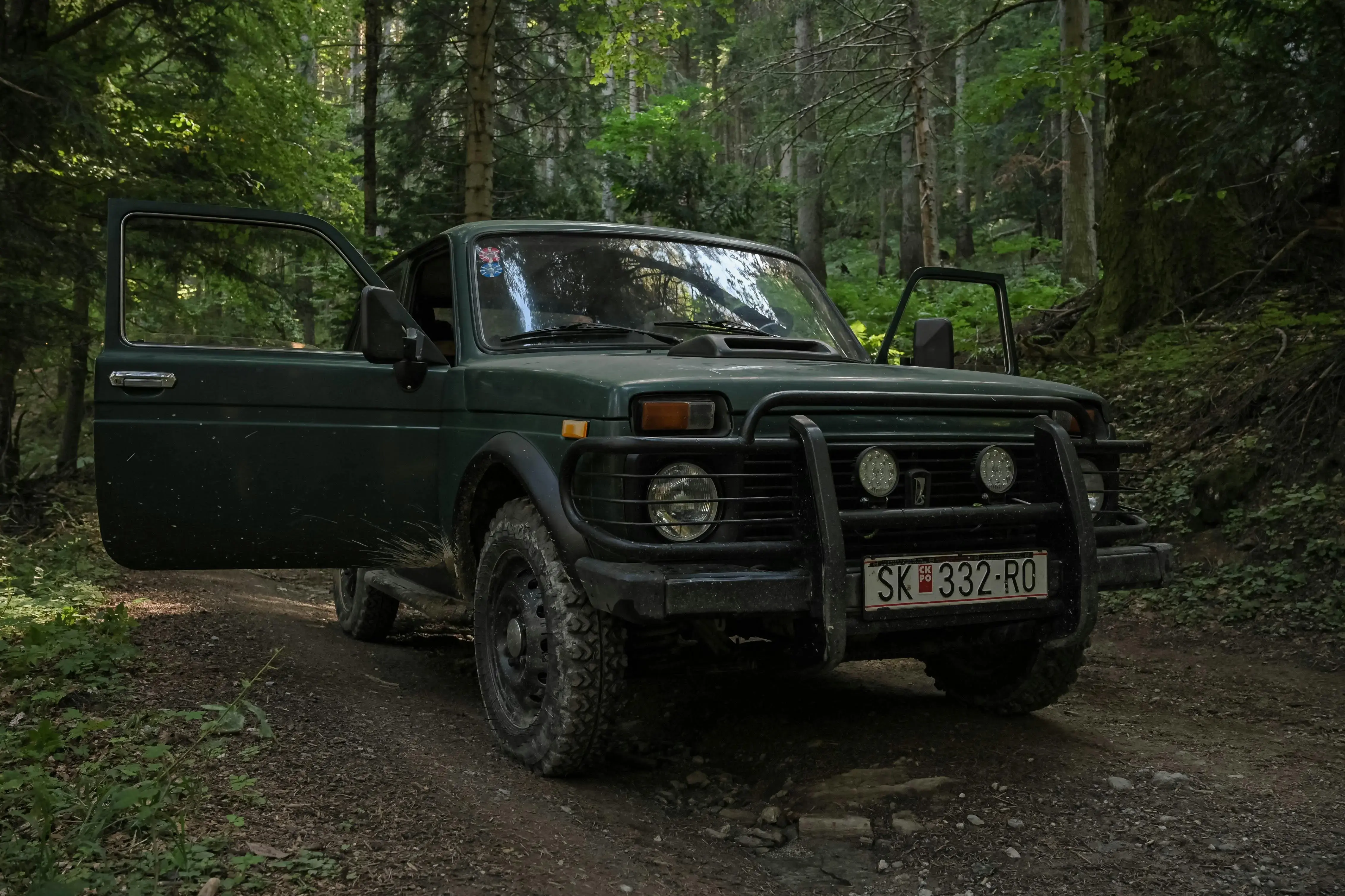 A dark green Lada Niva parked on a dirt trail 